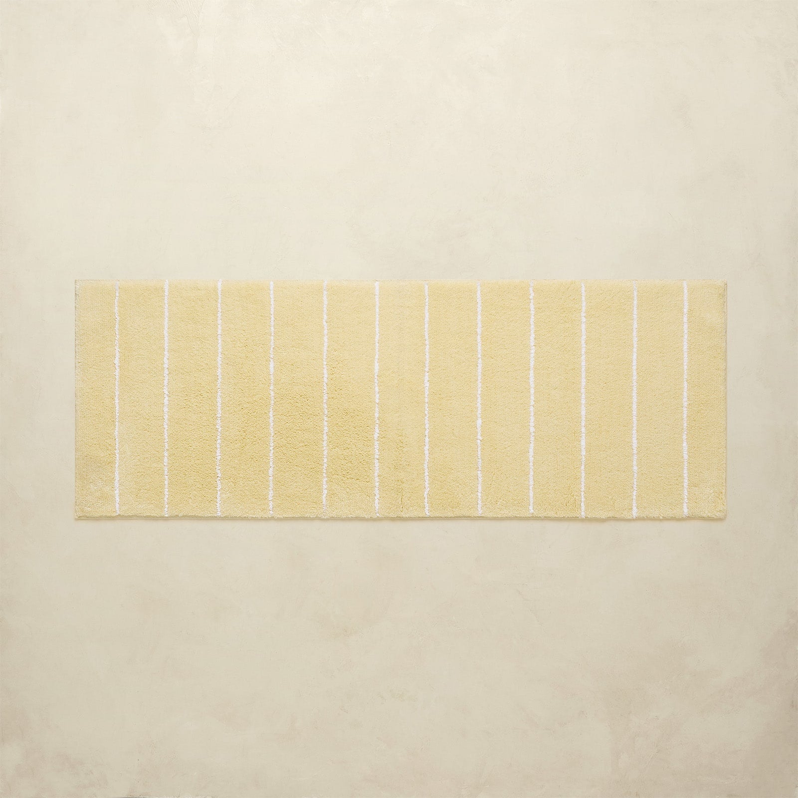 Rectangular yellow bath rug with white stripes on a beige background