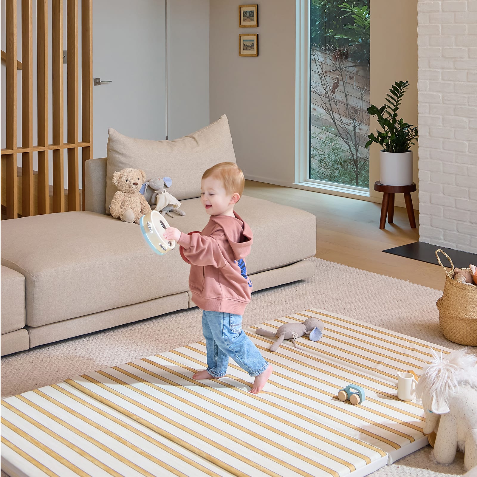 Child playing on a striped mat in a living room with toys and a couch.