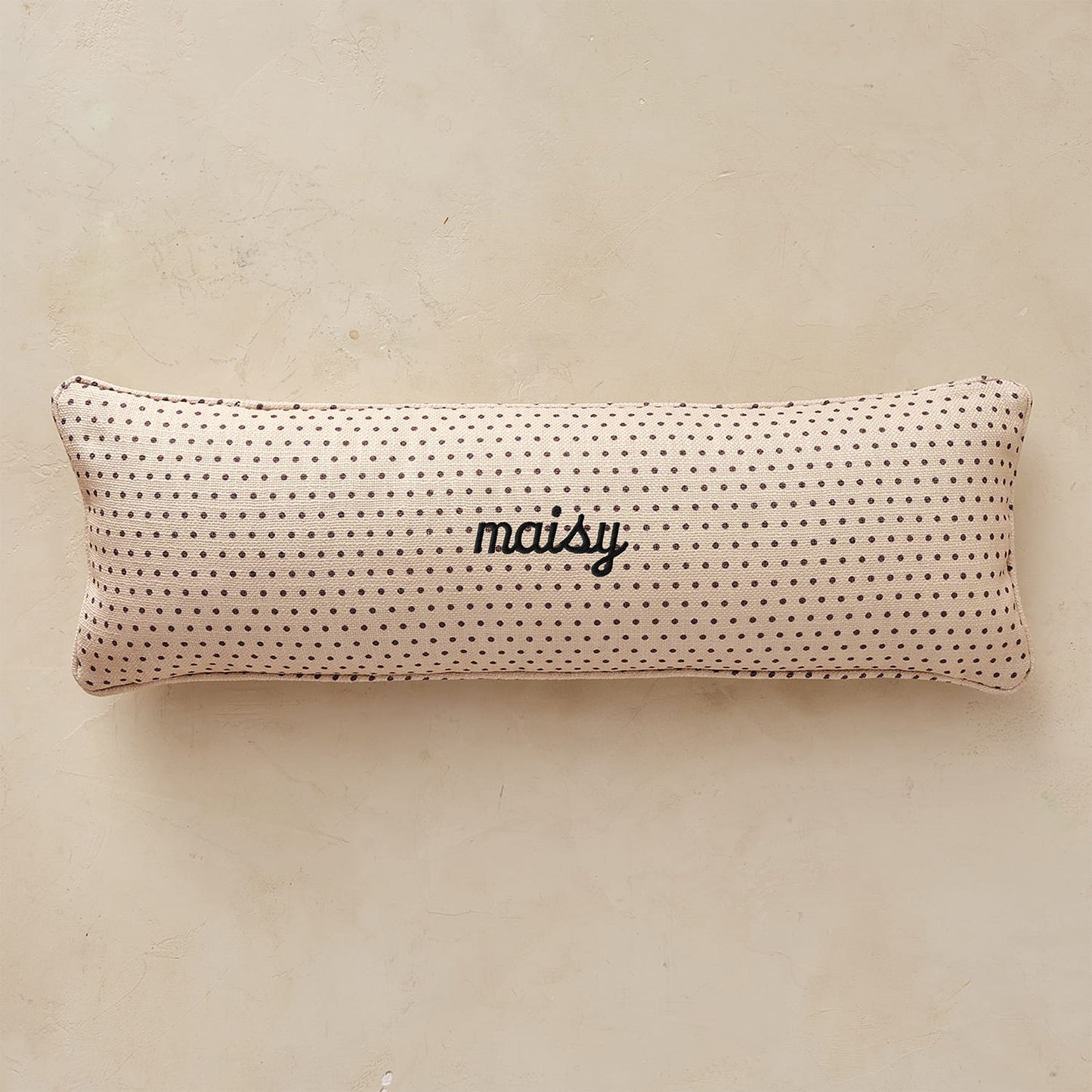 Rectangular pillow with black polka dots and 'maisy' text on a beige background