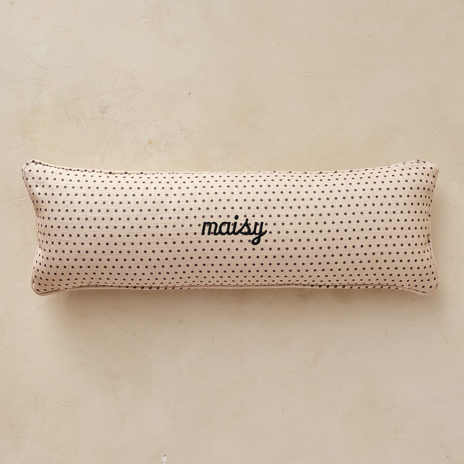 Rectangular pillow with black polka dots and 'maisy' text on a beige background