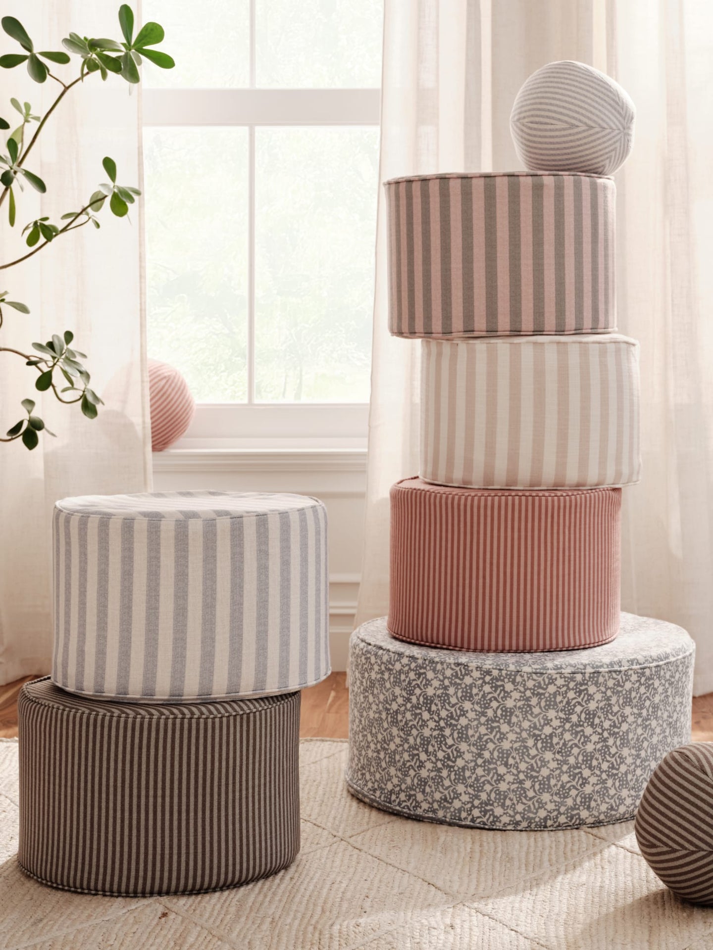 Stack of patterned ottomans on a light wooden floor with a plant and window in the background.