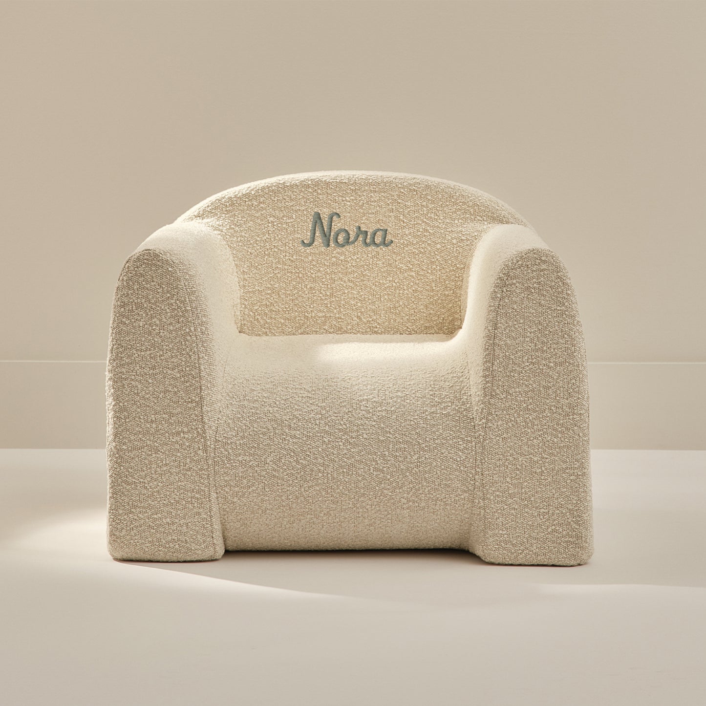 Beige textured armchair with 'Nora' embroidered on a beige background