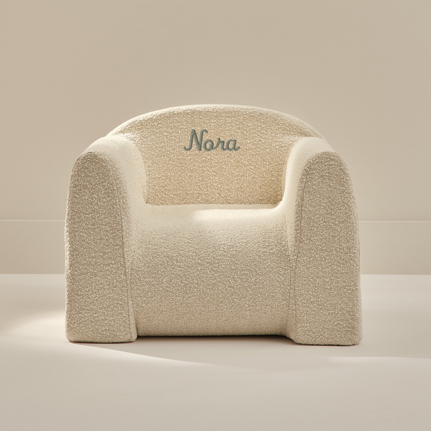 Beige textured armchair with 'Nora' embroidered on a beige background