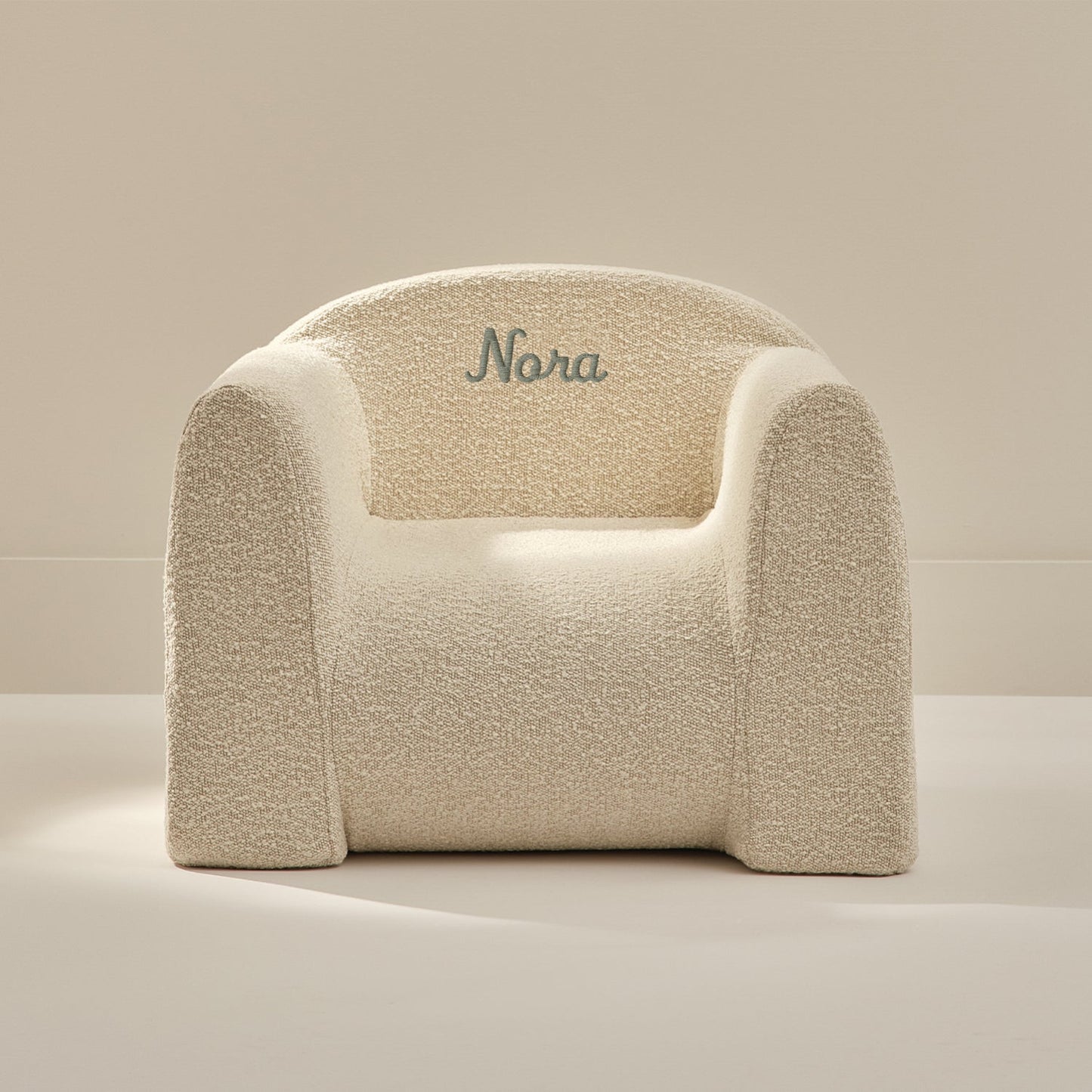 Beige textured armchair with 'Nora' embroidered on a beige background