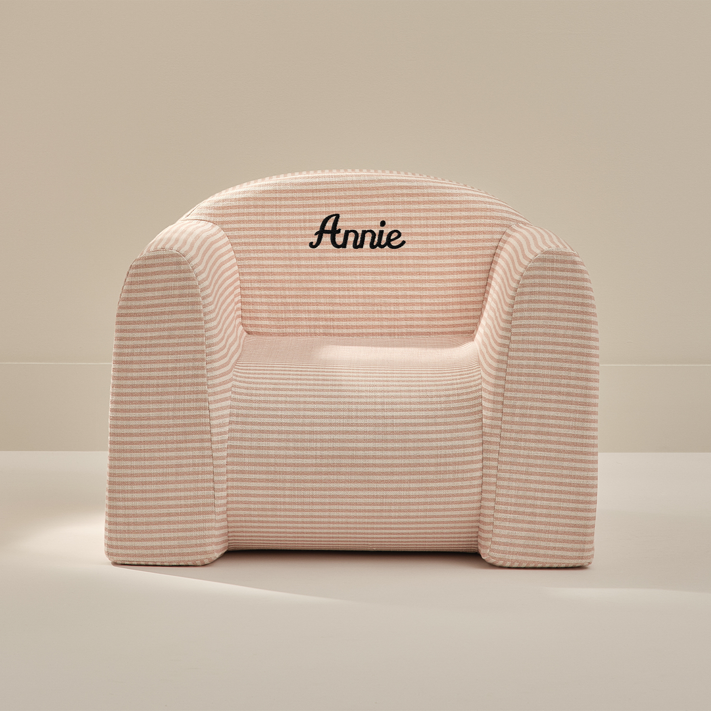 Pink armchair with 'Annie' embroidery on a beige background