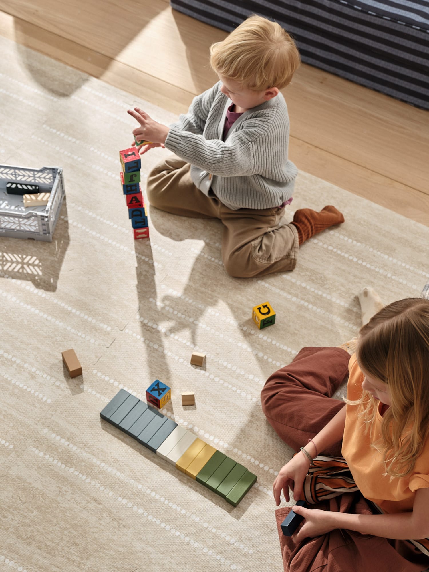Two children playing with colorful building blocks on a light wooden floor.