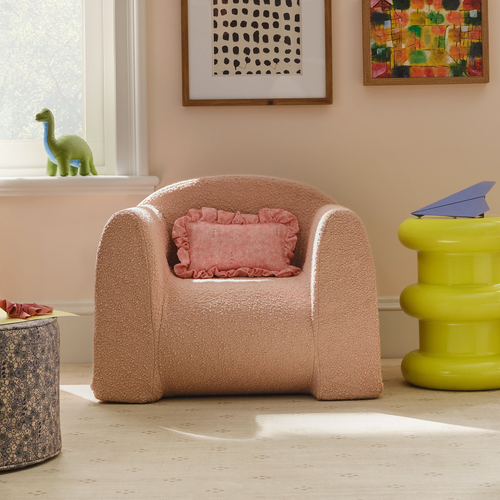Pink armchair with a pink pillow in a room with colorful abstract art on the wall.