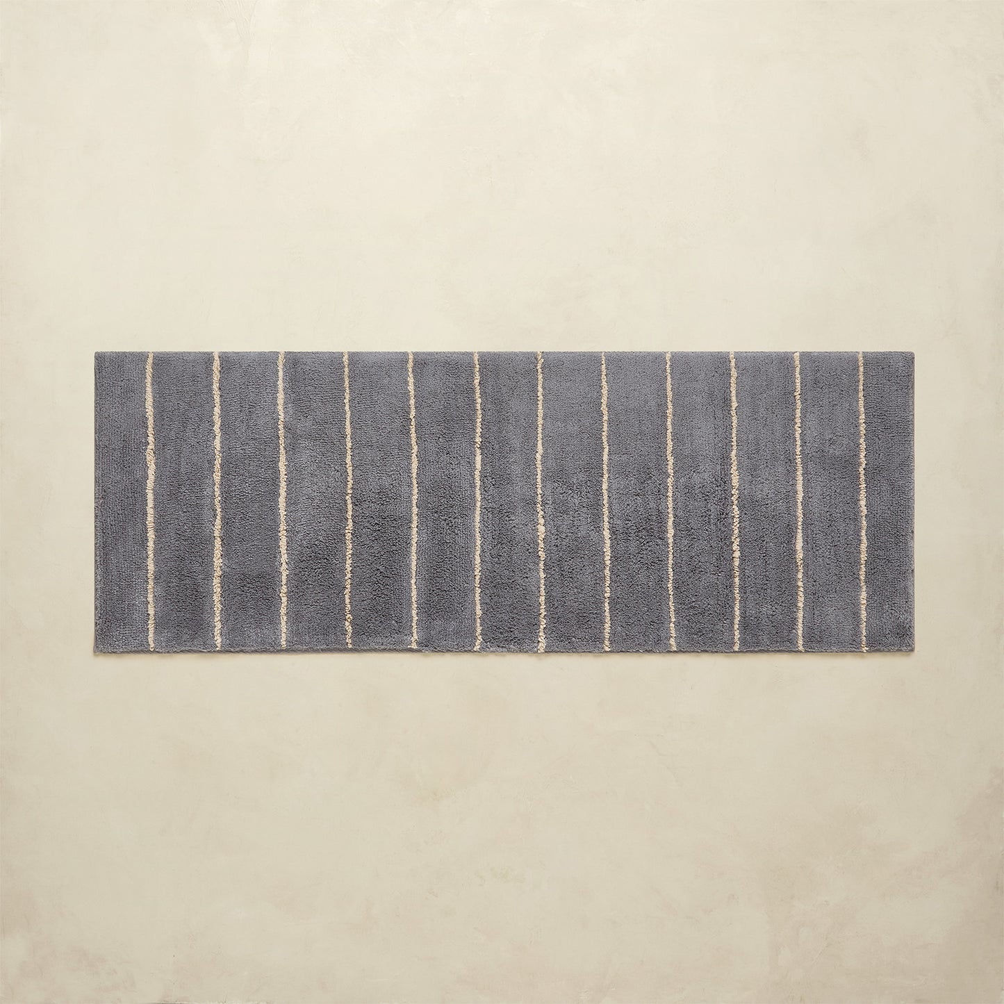 Rectangular blue and white striped bath rug on a beige background