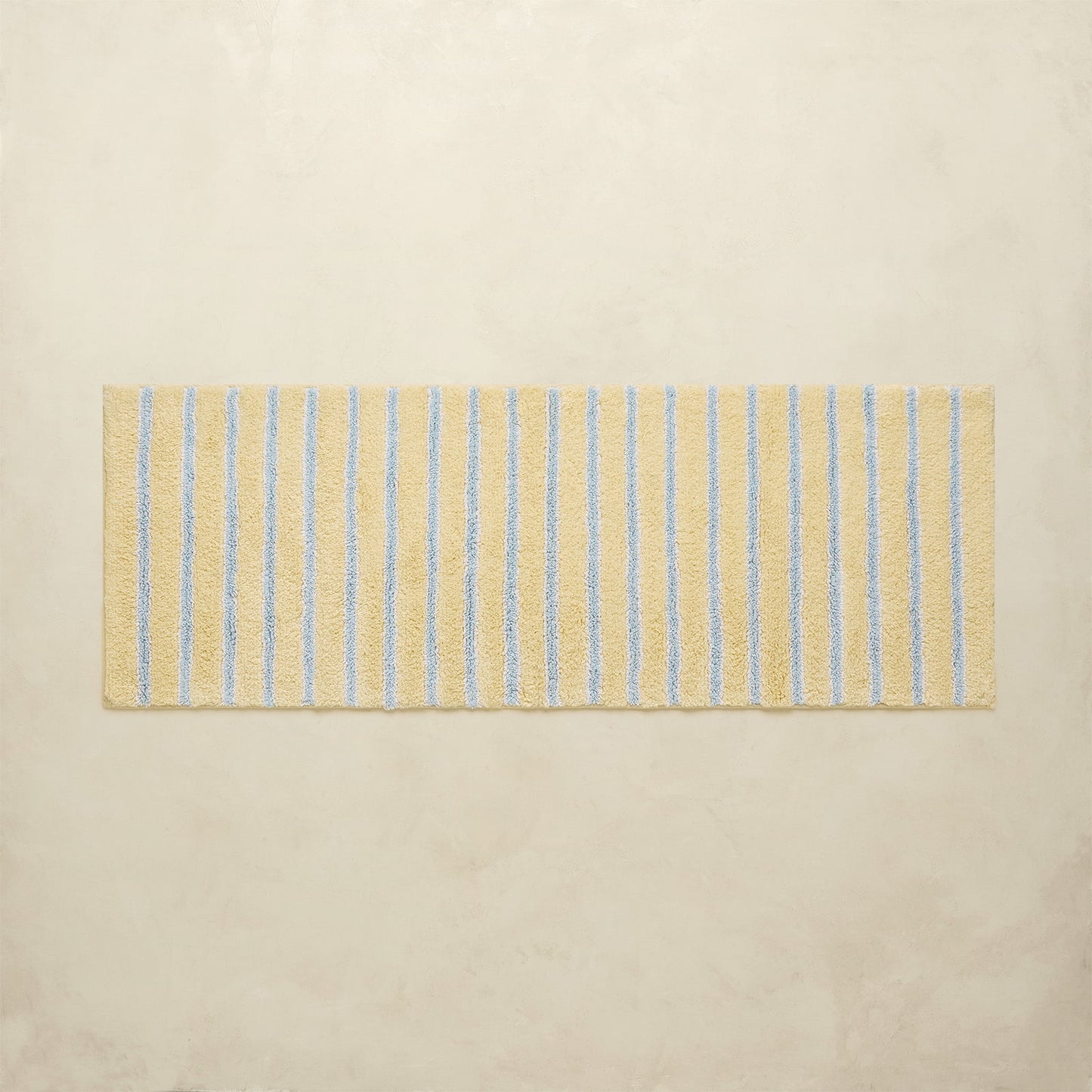 Rectangular bath mat with blue stripes on a beige background