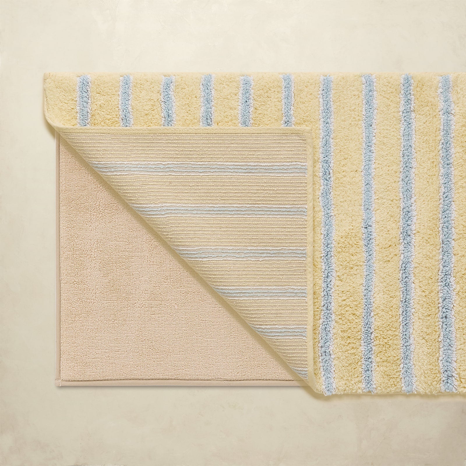 Beige bath mat with blue stripes on a beige background