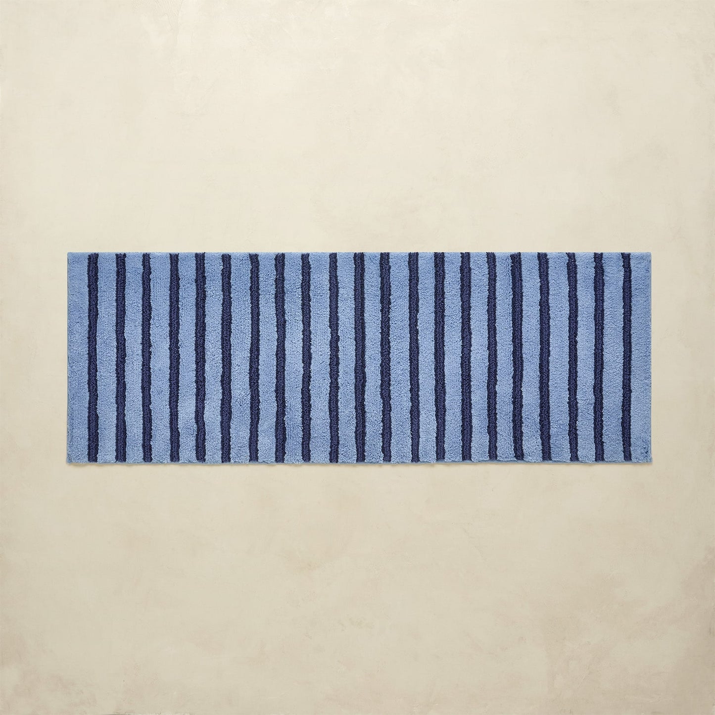 Rectangular blue and navy striped bath rug on a beige background