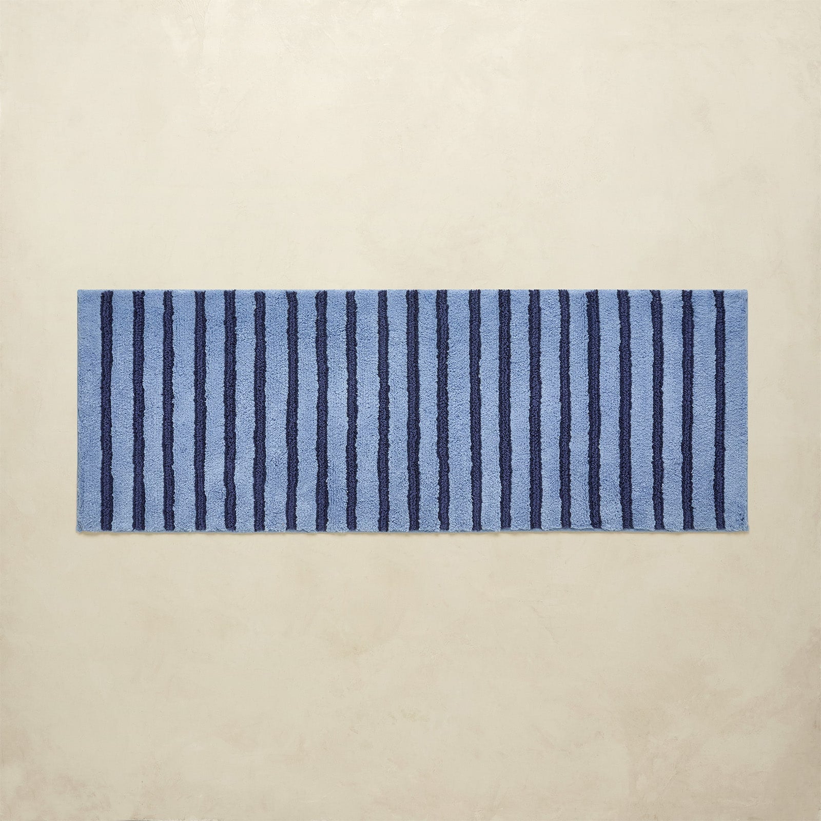 Rectangular blue and navy striped bath rug on a beige background