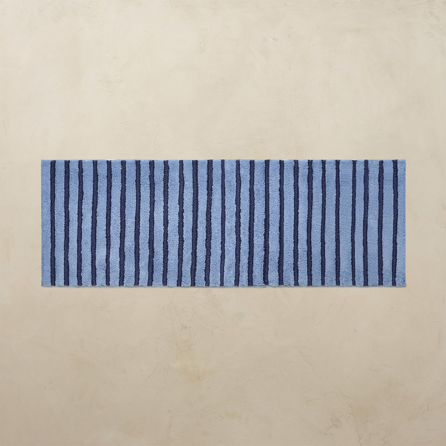 Blue and navy striped bath rug on a beige background