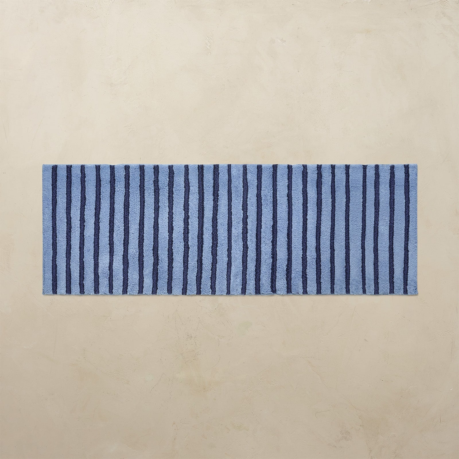 Blue and navy striped bath rug on a beige background