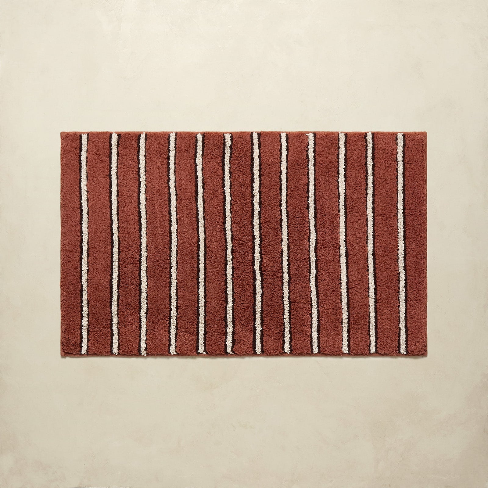 Rectangular bath mat with red and white vertical stripes on a beige background