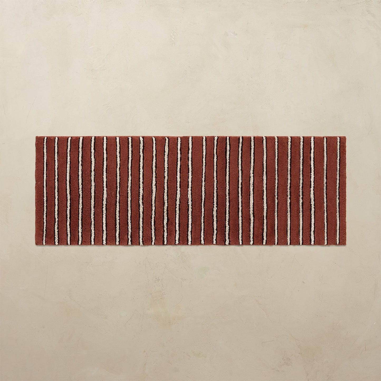 Rectangular red and white striped bath rug on a beige background