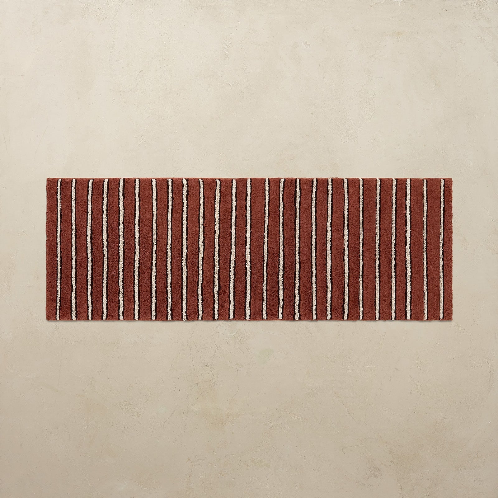 Rectangular red and white striped bath rug on a beige background