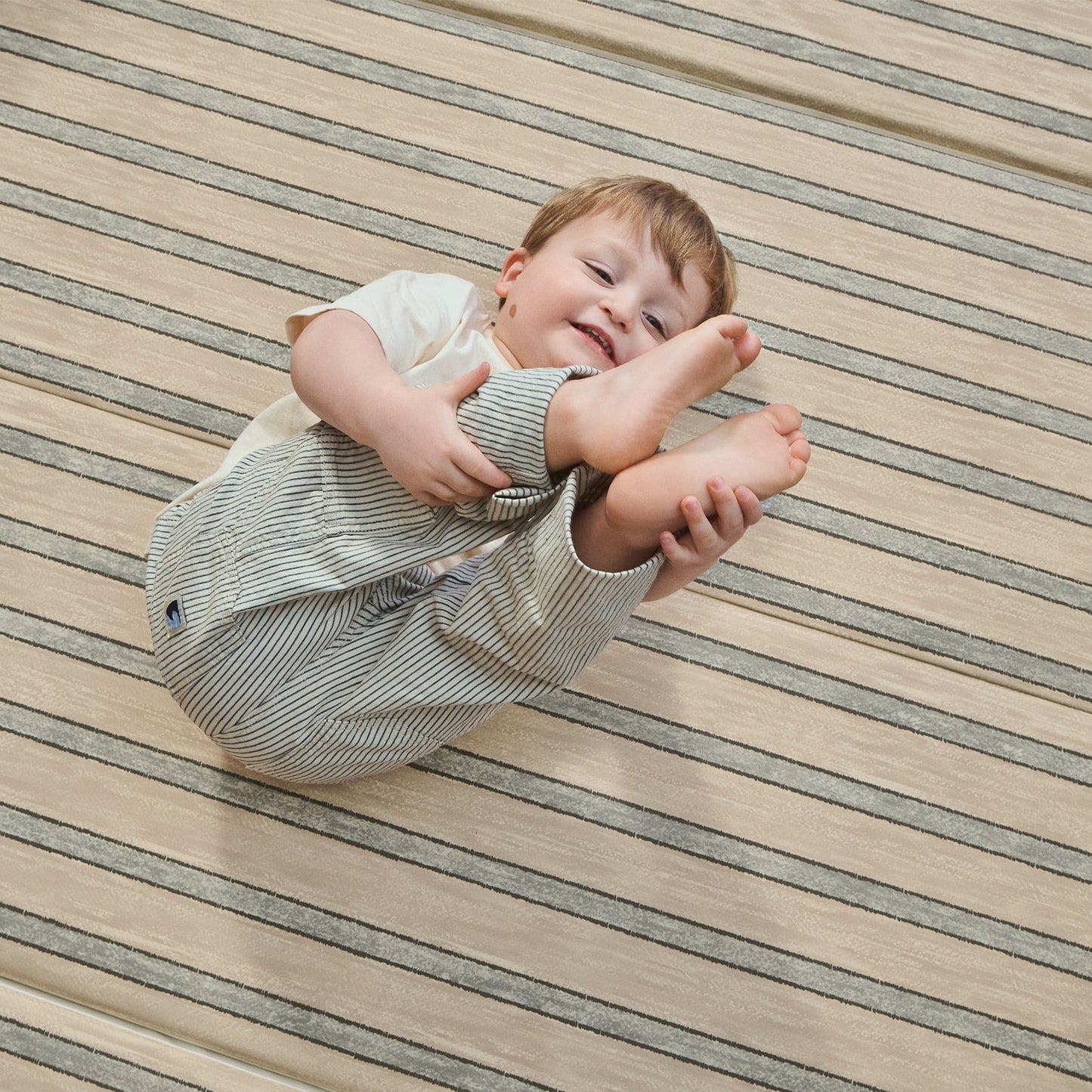 Child in lying on a beige striped tumbling mat 