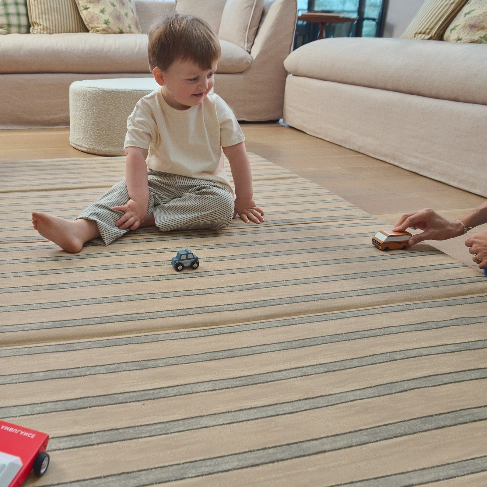 Child playing with toy cars on a striped tumbling mat in a living room.