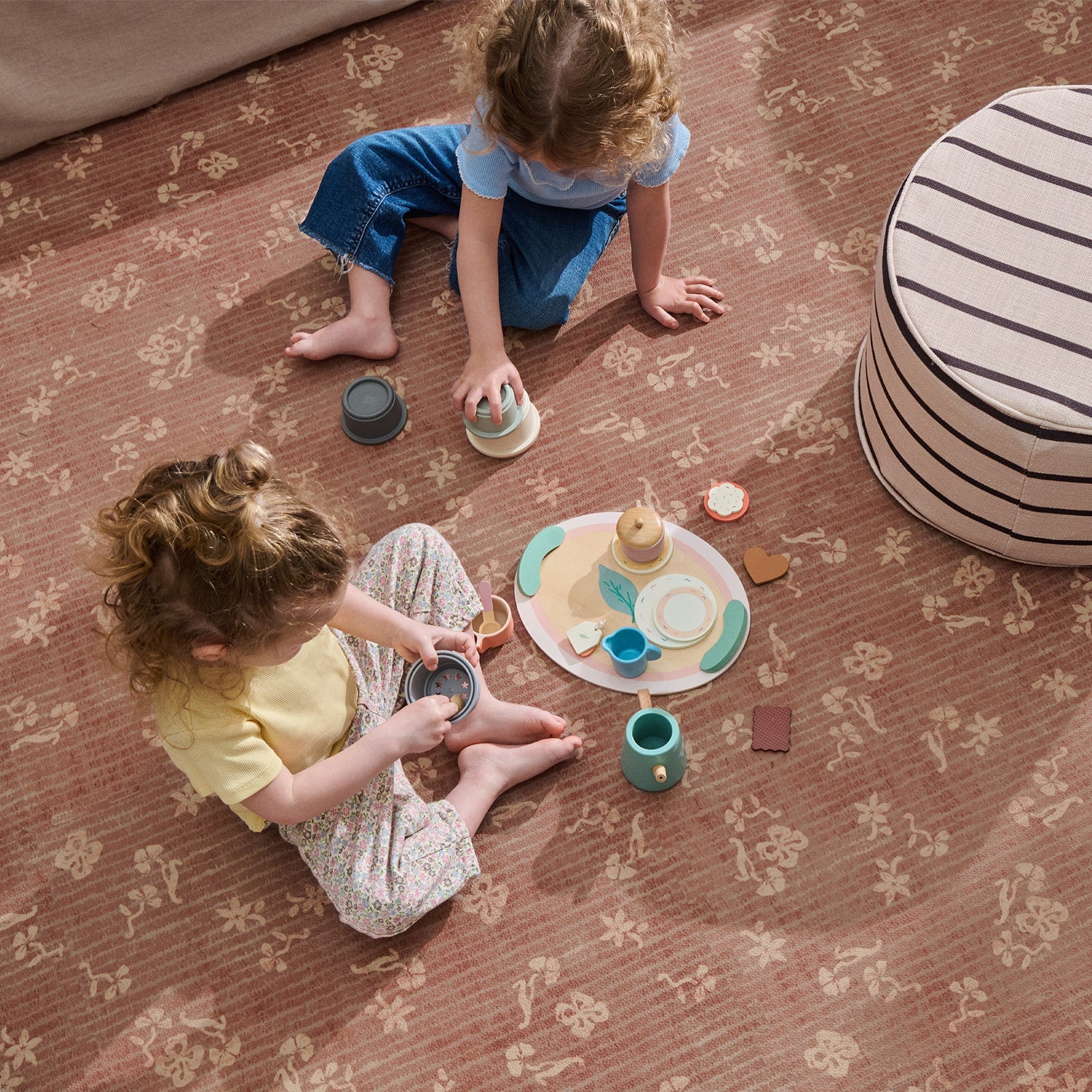Two children playing with toy tea sets on a patterned floor.