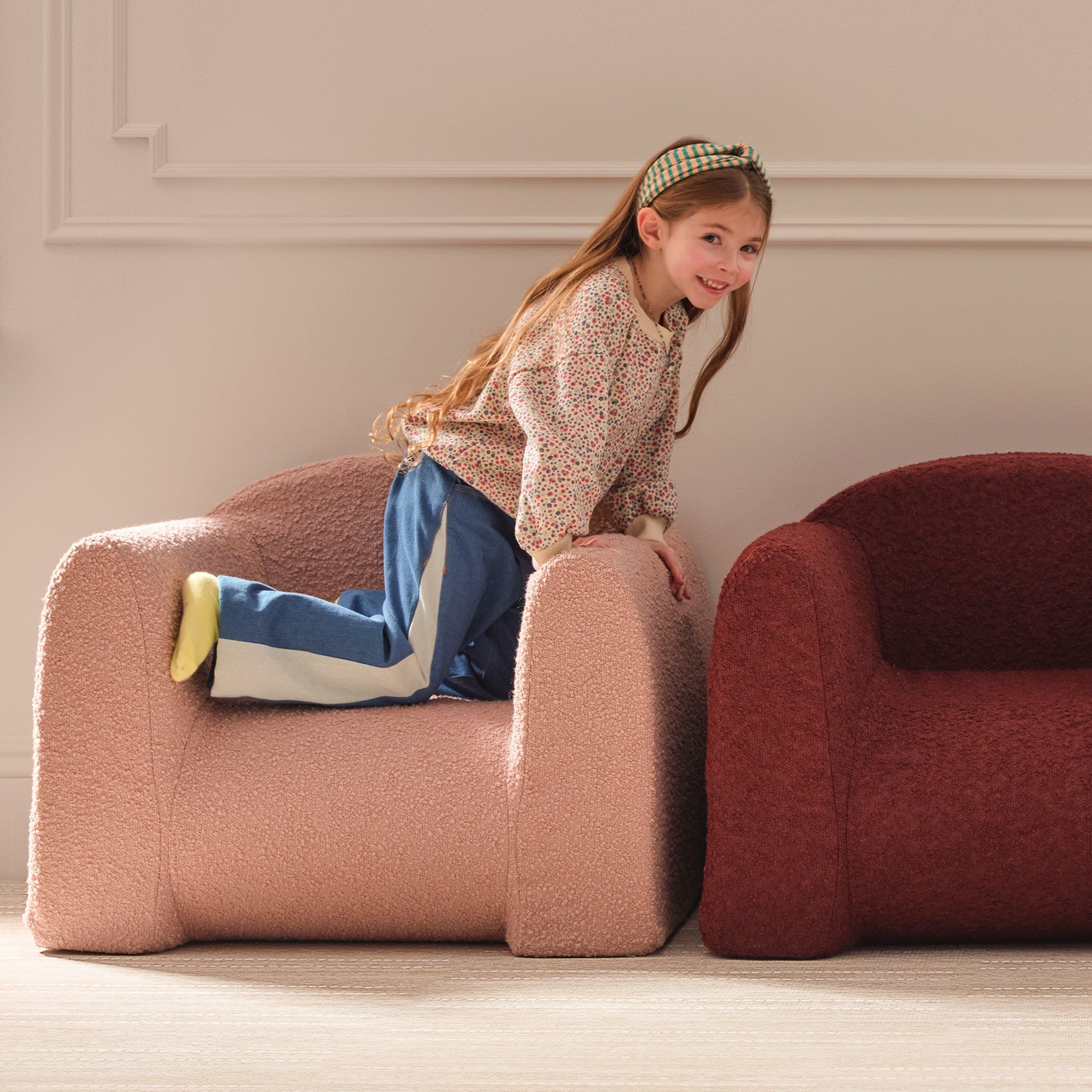 Young girl sitting on a pink armchair in a room with a neutral color scheme