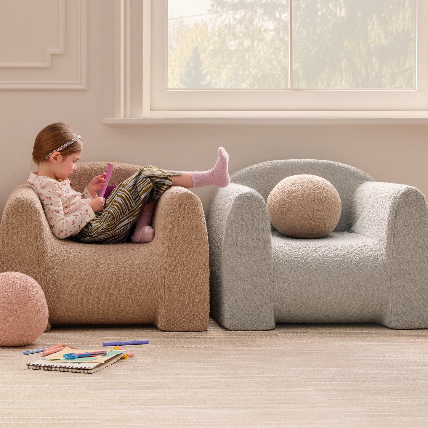 Child sitting on a beige armchair in a room with large windows.