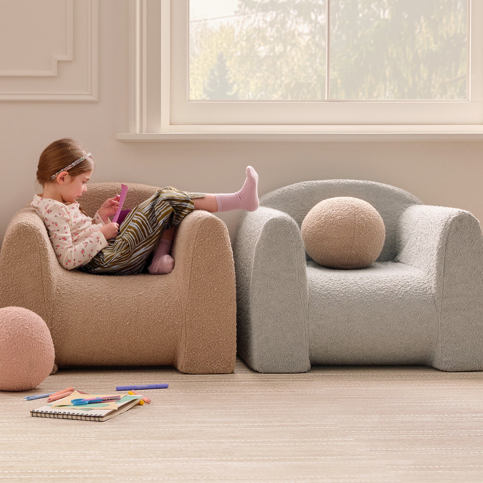Child sitting on a beige armchair in a room with large windows.