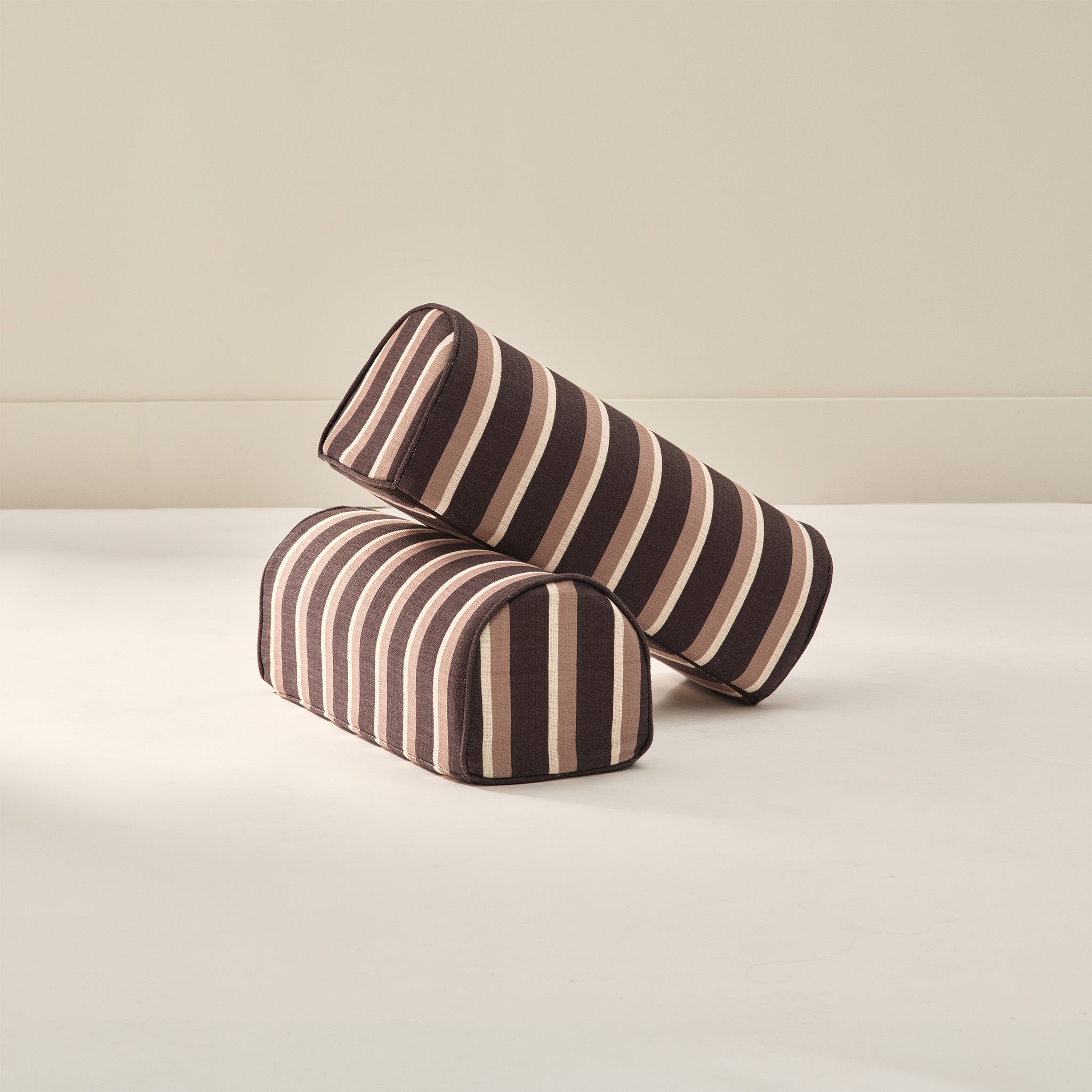 Two striped patterned arch cylindrical armrest pillows from House of Noa in brown and cream
