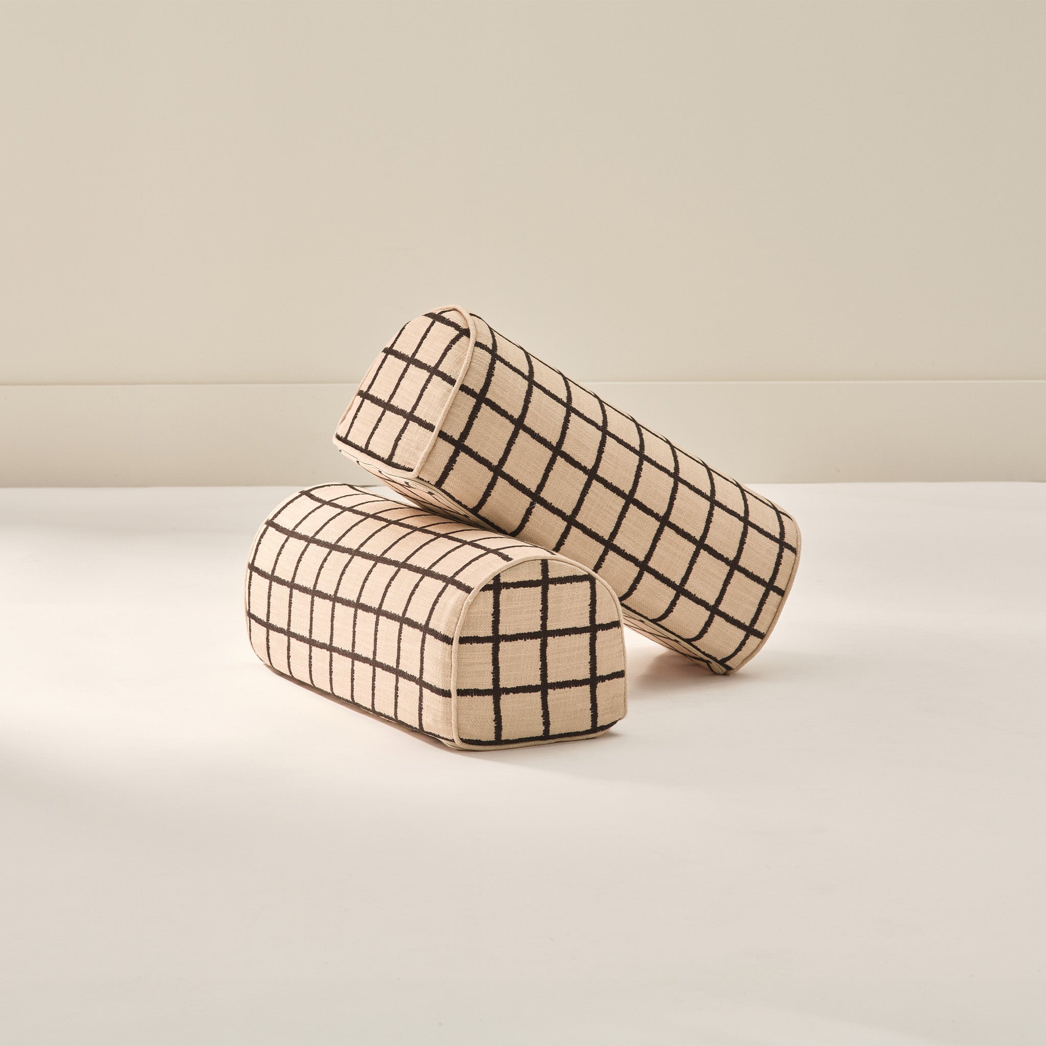 Two grid patterned arch cylindrical armrest pillows from House of Noa in wheat and sable from House of Noa