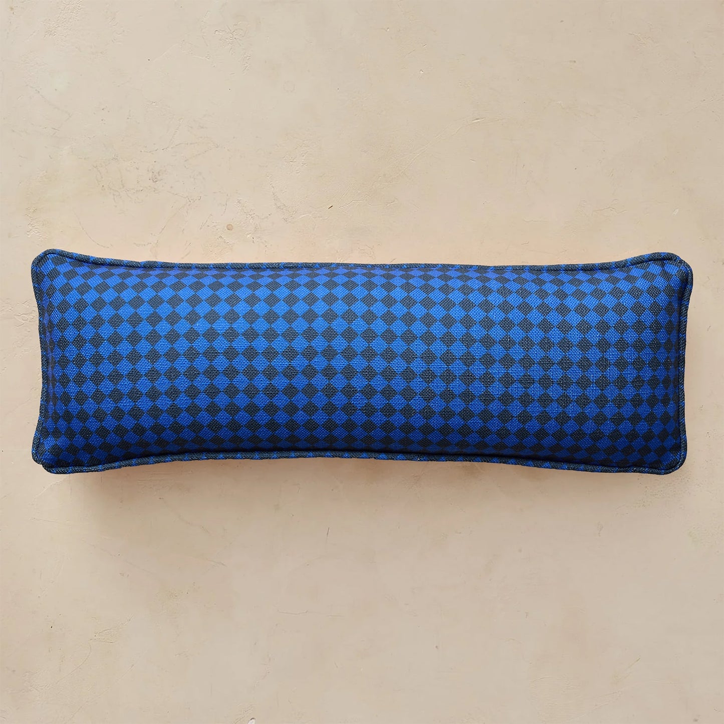 A rectangular lumbar pillow with a blue and black checkered pattern, displayed against a neutral beige background.