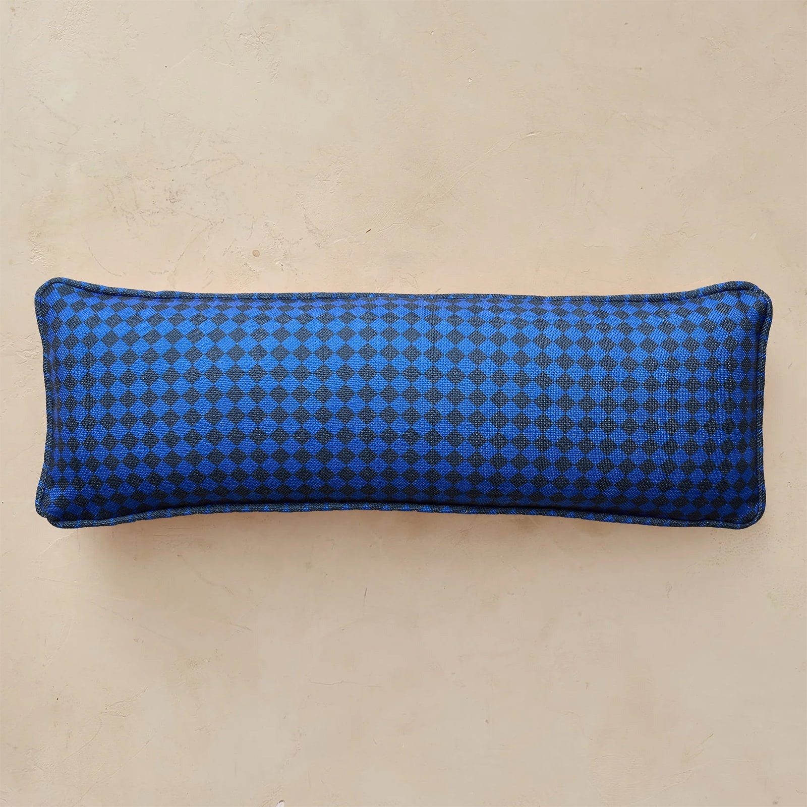 A rectangular lumbar pillow with a blue and black checkered pattern, displayed against a neutral beige background.