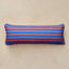 A rectangular lumbar pillow with horizontal stripes in royal blue and orange, resting on a textured beige surface.
