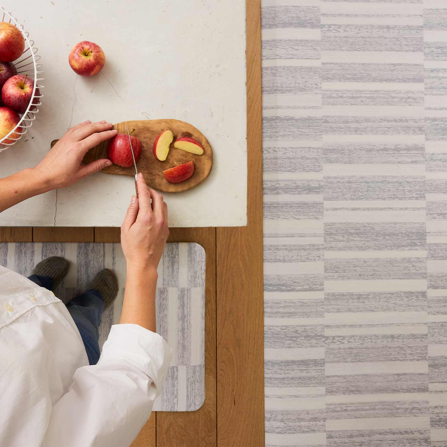 sutton stripe heather gray inverted stripe standing mat shown from in sizes 22x54 and 30x108 with woman standing on the mat at kitchen counter cutting apples