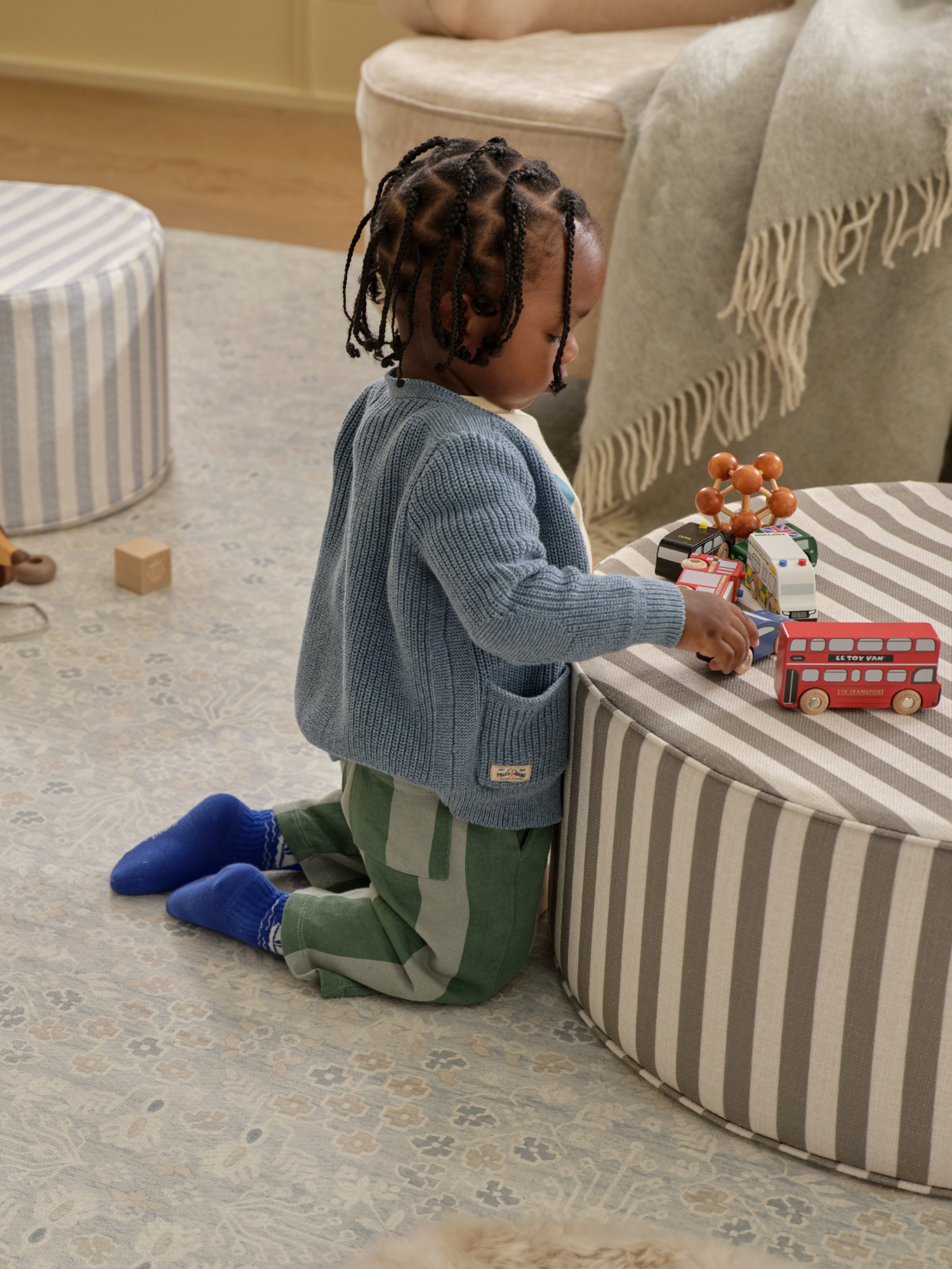 Child kneeling on a play mat playing with toys on a striped ottoman in a living room