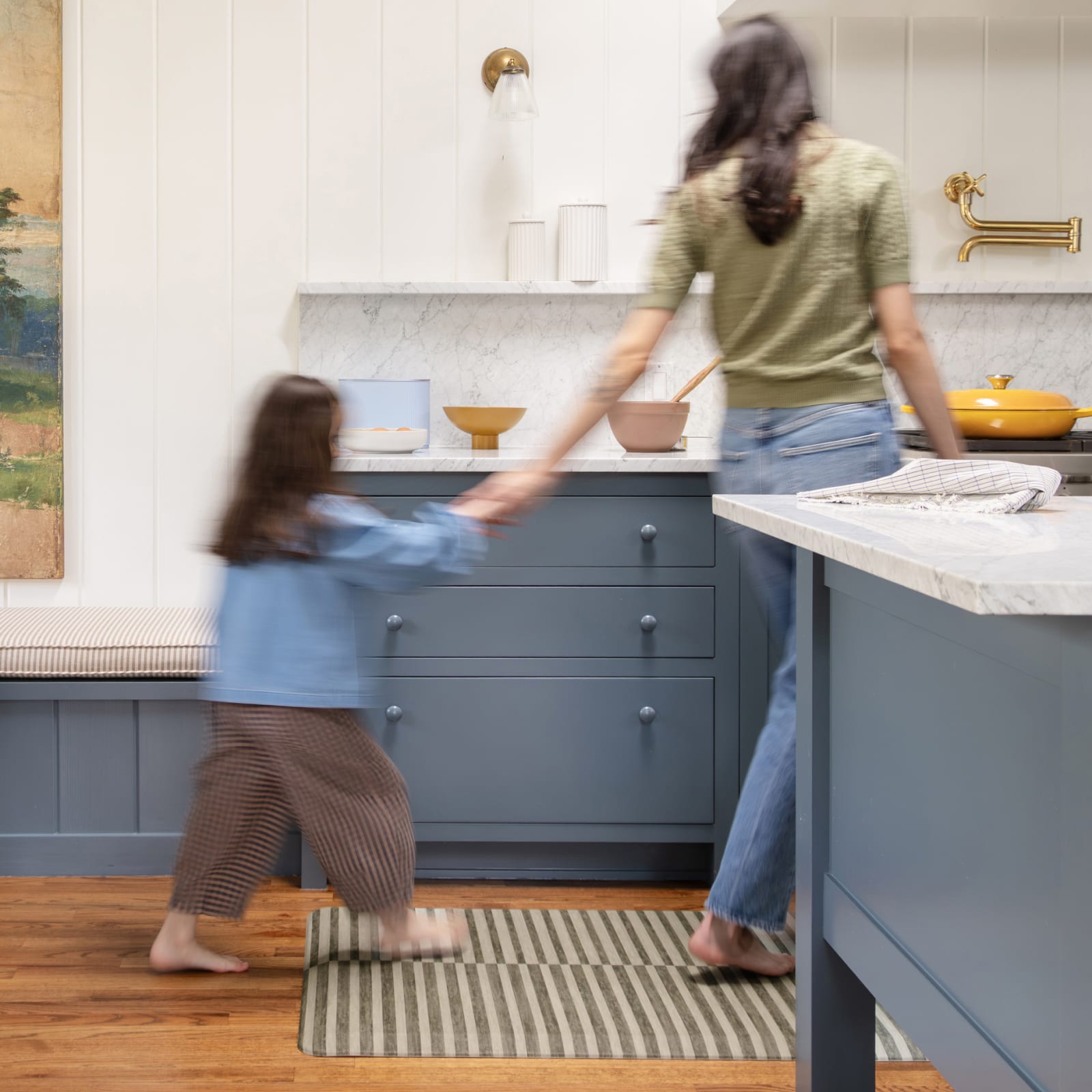 Woman and child in a kitchen with blue cabinets and white countertops.
