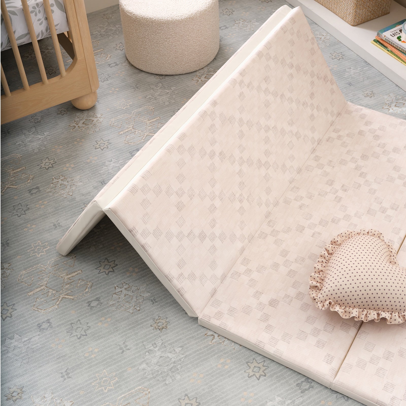 Baby folding play mat with textured surface on a blue mat, next to a crib and cushion.