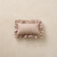 A small rectangular ruffled pillow in a dusty pink fabric with white polka dots, centered on a textured beige background.