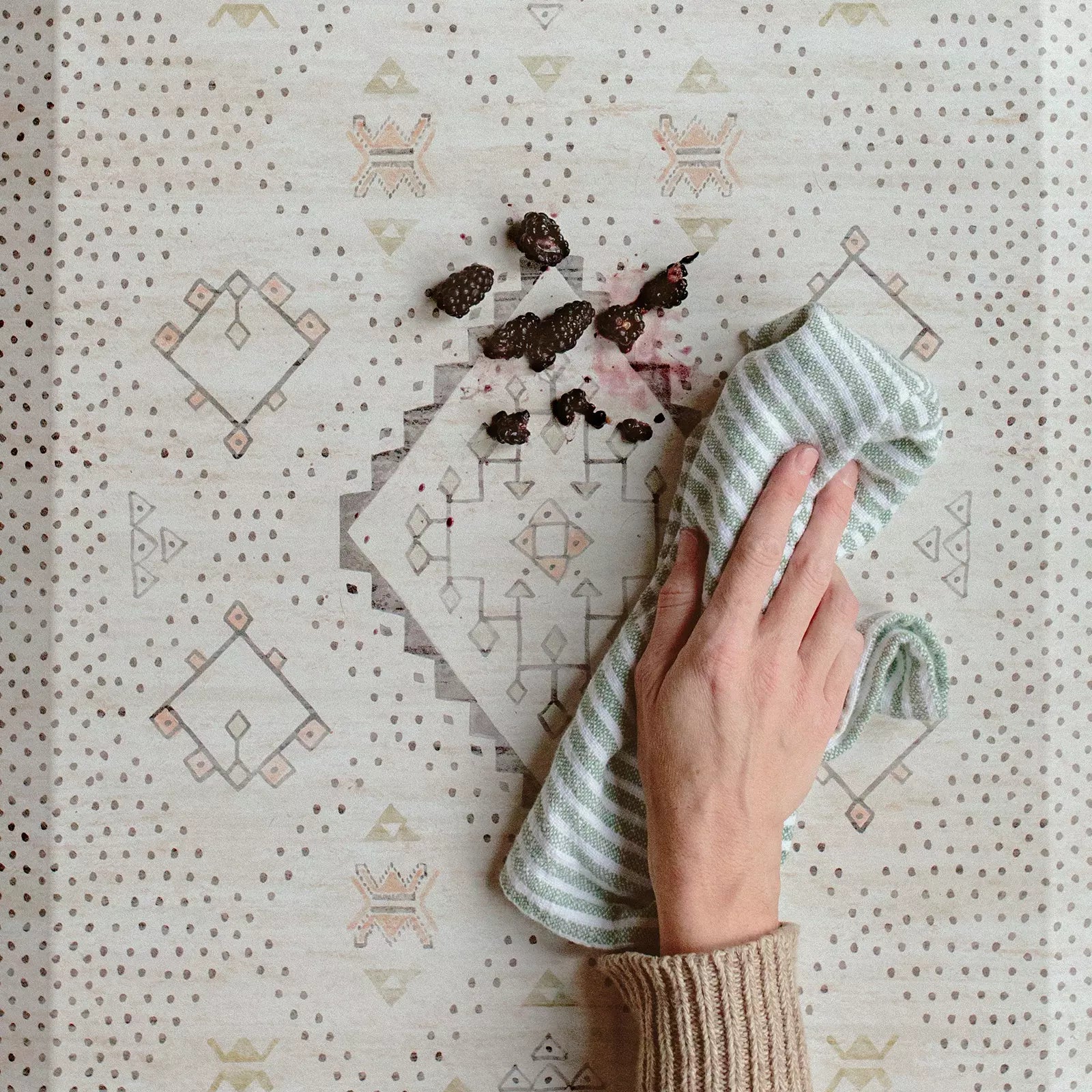 Nama Standing Mat in Ula Oat neutral boho print. Anti-fatigue kitchen mat shown close up with a hand wiping up a spill with a cloth.