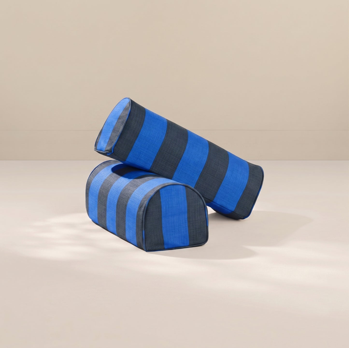 Two cylindrical armrest pillows with blue and dark gray horizontal stripes, displayed on a neutral beige surface.