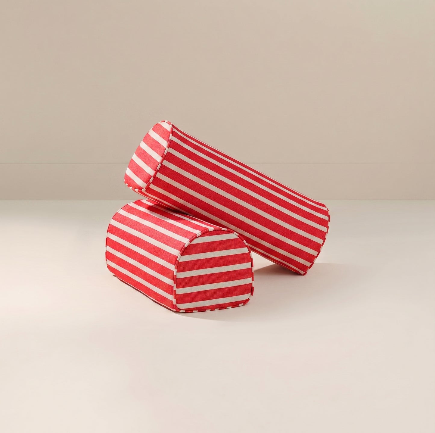 Two cylindrical red and white striped fabric armrests on a light beige studio background.