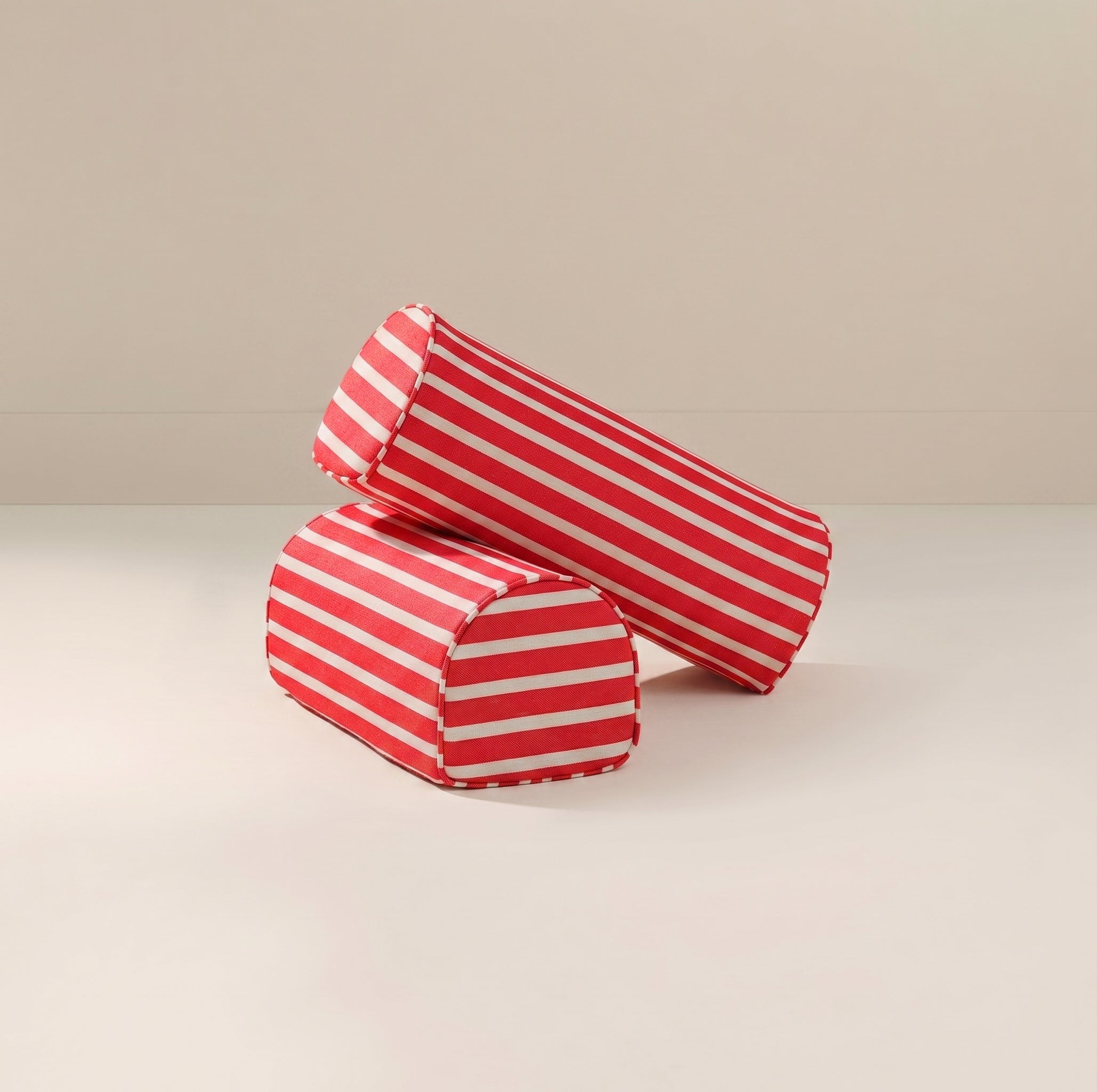 Two cylindrical red and white striped fabric armrests on a light beige studio background.