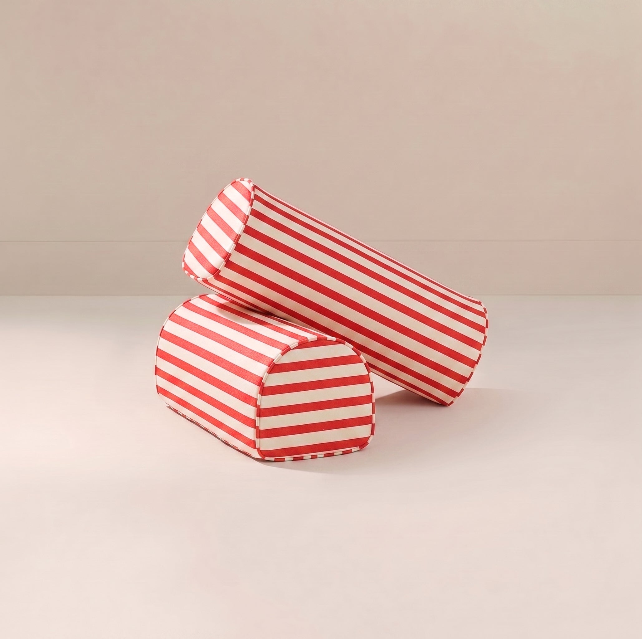 Two cylindrical red and white striped fabric armrests upright on a light beige surface against a matching beige background.