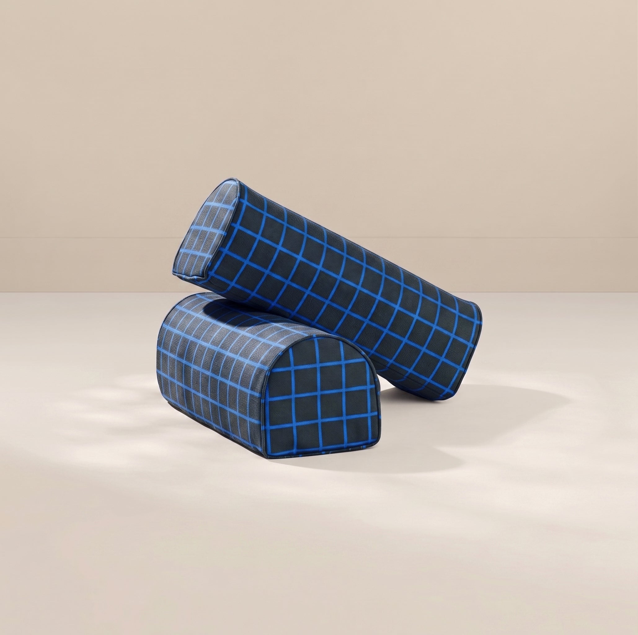 Two cylindrical armrest pillows with a blue and black grid plaid pattern, stacked on a light beige surface against a matching beige background.