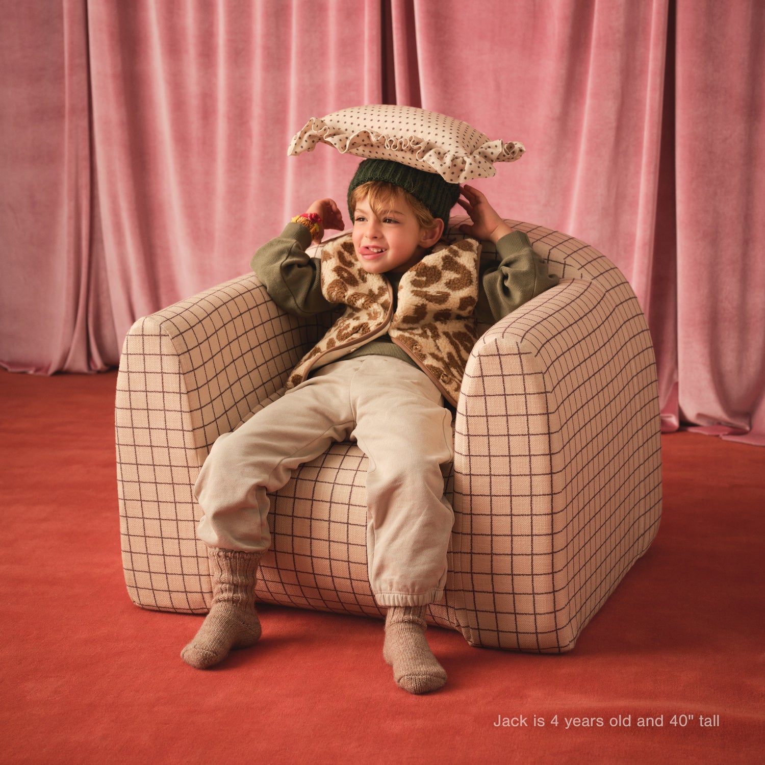 Child sitting on a checkered chair with pink curtains in the background
