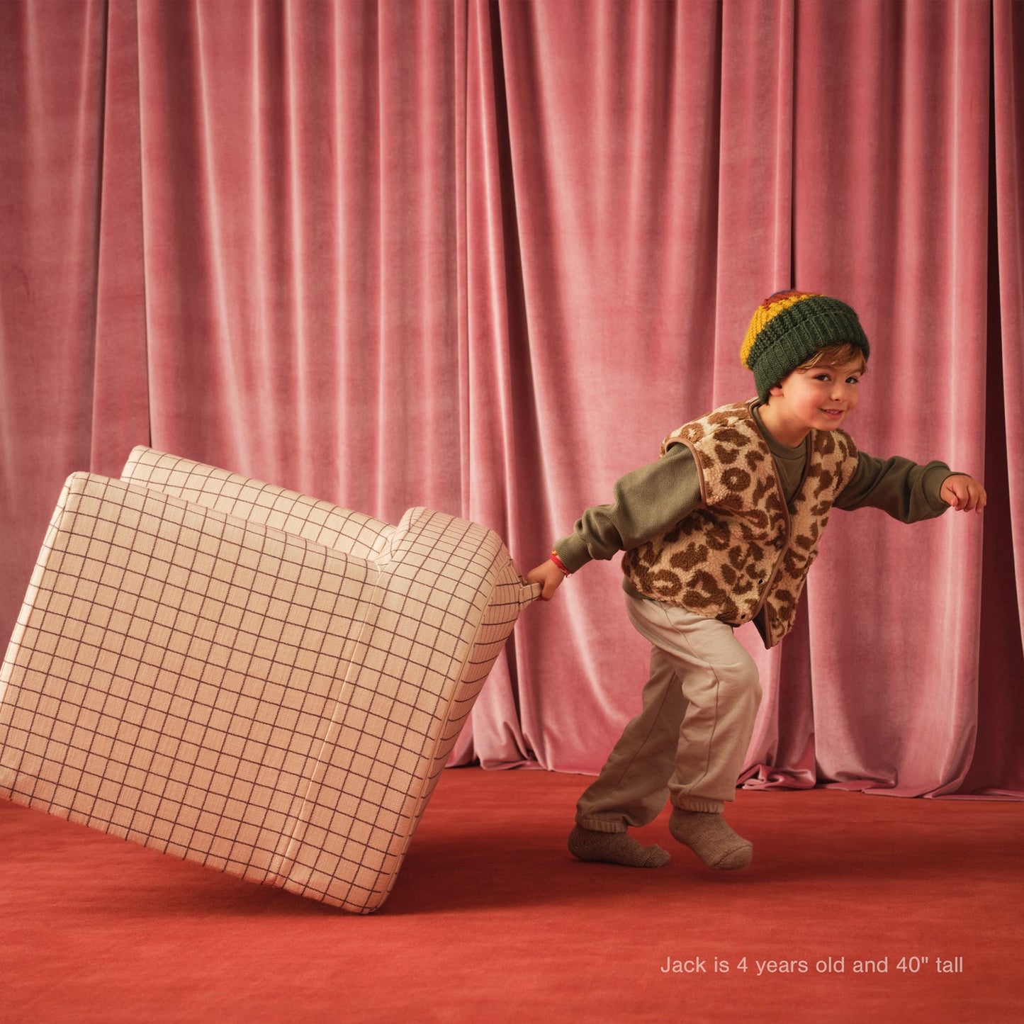 Child pulling a suitcase on a stage with pink curtains