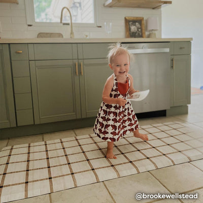 Brown and white minimal line print kitchen mat shown in kitchen with baby laughing and eating a snack.