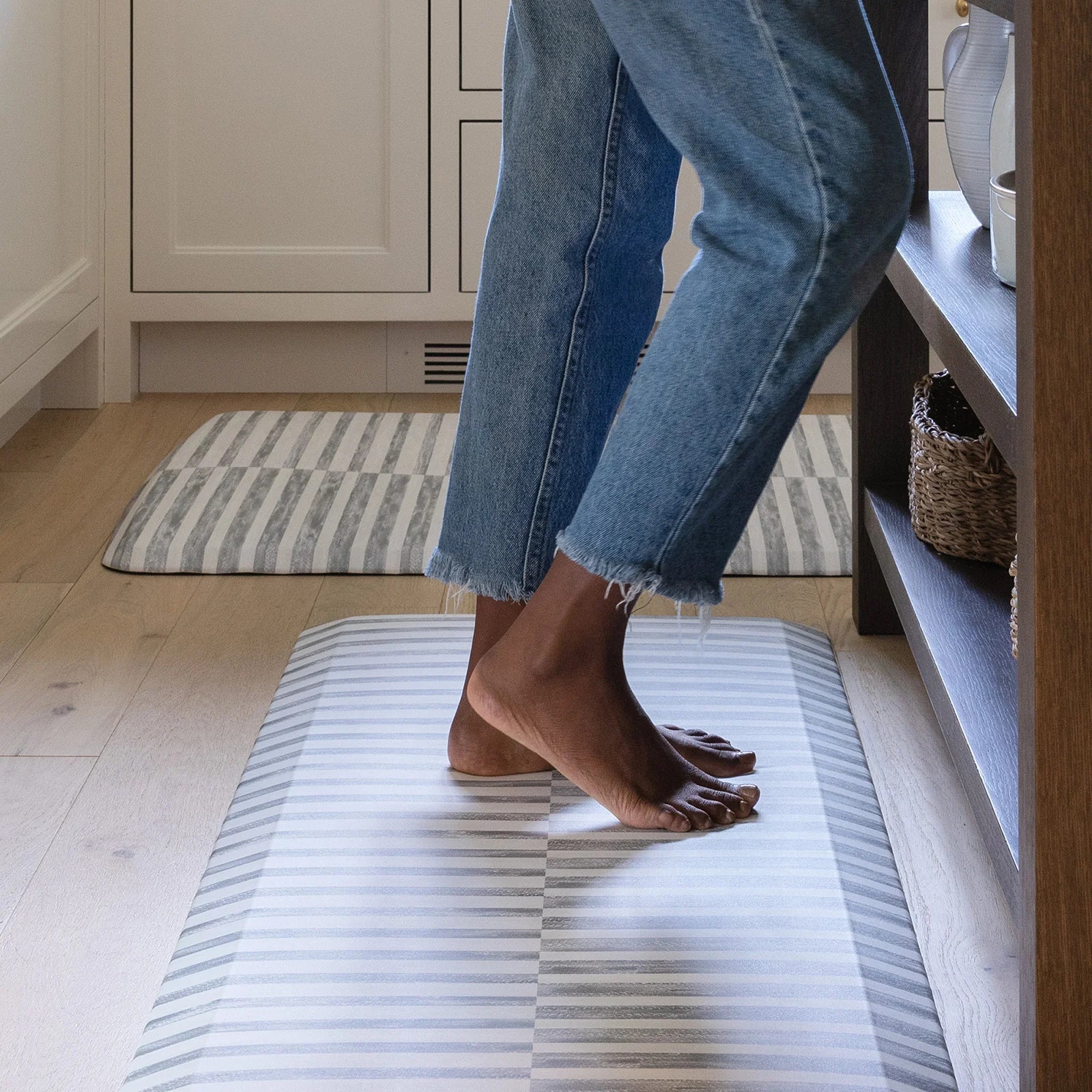 Reese pewter gray and white inverted stripe standing mat shown with woman's feet standing on the mat in a kitchen