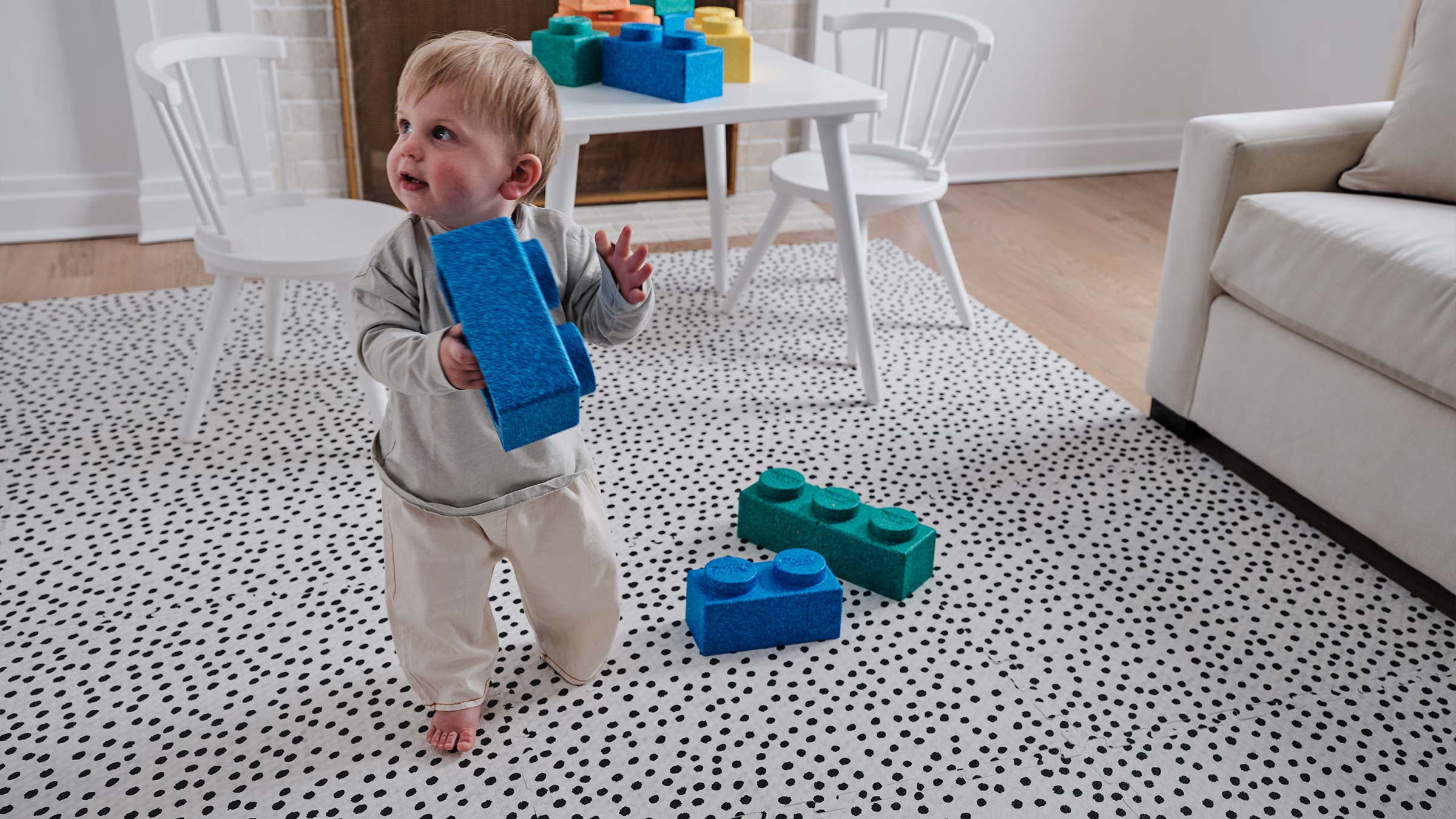 Apollo pepper black and white polka dot play mat shown in living room with baby carrying lego blocks