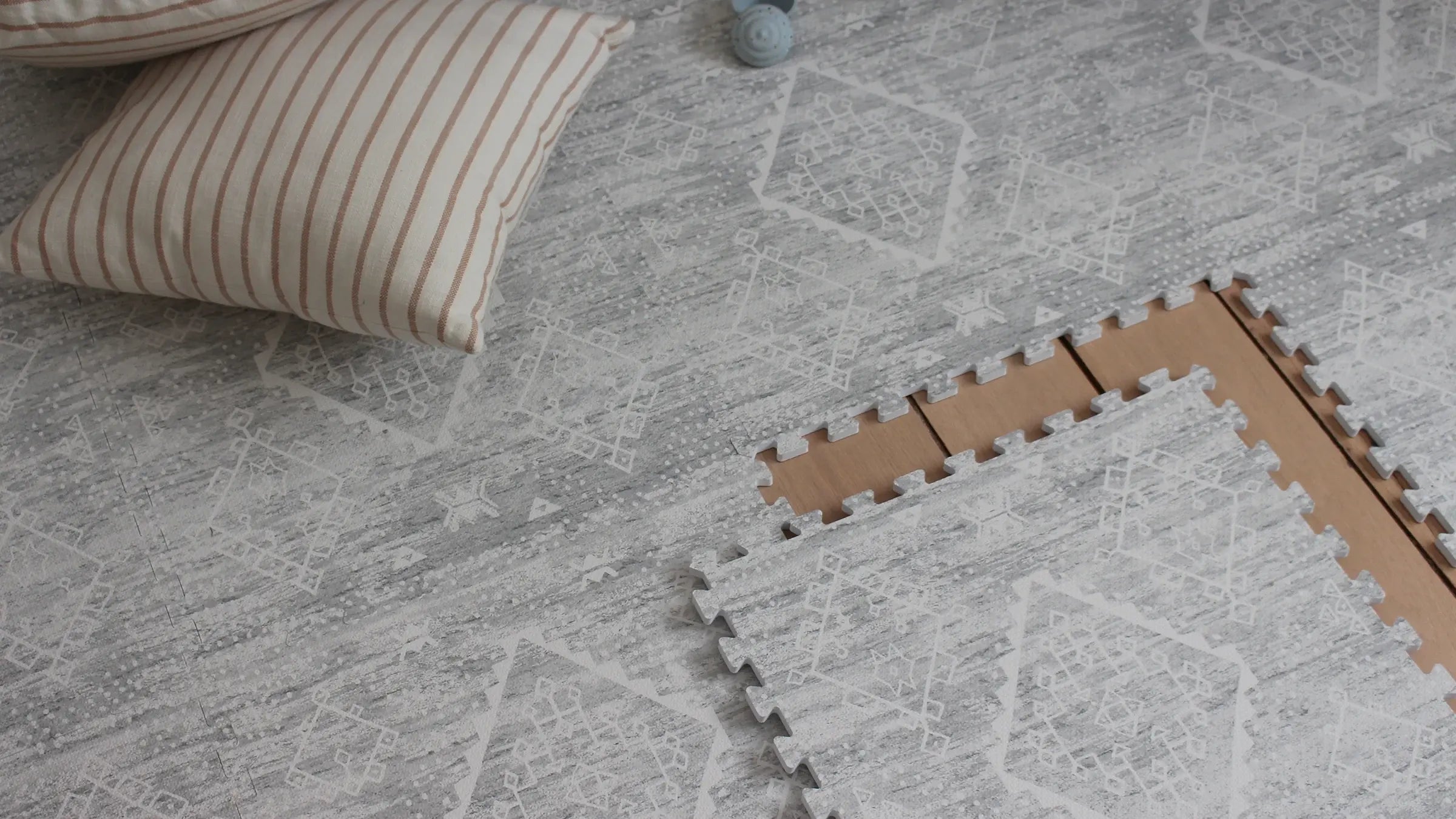 Ula gray boho pattern play mat with 1 tile exposed and tan and white stripe pillow on the mat