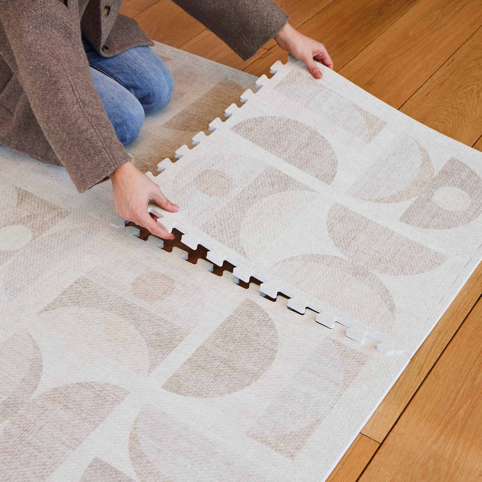 Luna sandstone neutral geometric print play mat on wooden floors with woman putting the corner tile in place